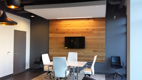 A conference room with custom wood panel on the wall behind a monitor screen. A square white table with 4 white chairs are in the center of the room.