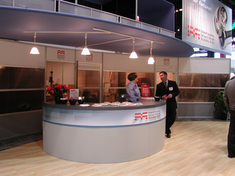 Custom round reception desk at trade show for Methods Machine Tools Inc. A large sign with logo and tools hangs next to the desk.
