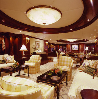 Sitting room with dark wood coffee tables and yellow checkered armchairs. A couch with throw pillows to the left, and custom woodwork on the ceiling and surrounding walls.