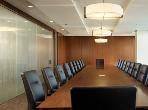 Large wooden conference room table With hanging lighting, brown leather chairs and frosted glass walls and door.
