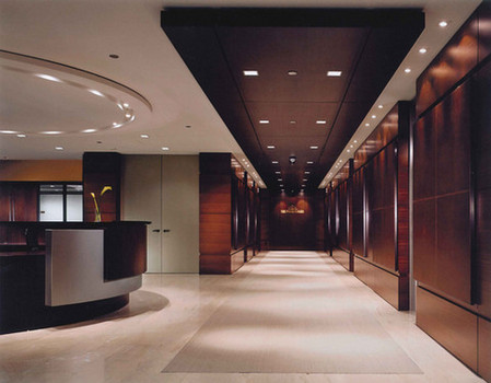 Large open reception area inside office building. A long hallway with overhead recessed lighting and round reception desk to the left.