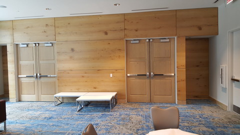 Gathering room in the Renaissance hotel with blue carpet, two double-doors and custom wood panels on the wall.