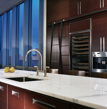 Example of Bernard Woodwork in a custom kitchen. A white marble countertop with sink and decorative fruit. On the far wall, appliances are set into dark woodword with a wine fridge and ladder to reach upper storage cabinets.